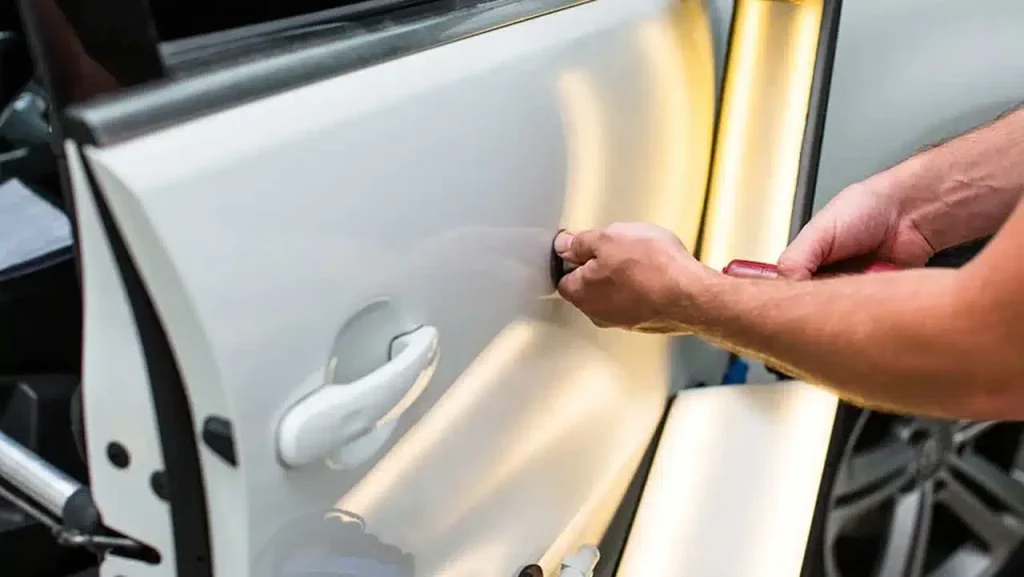 A mechanic using a tool to repair a dent in a car door.