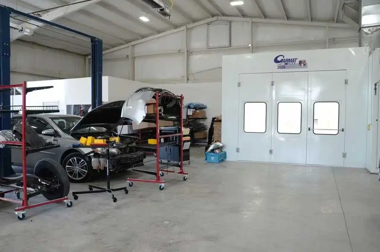 Interior of a professional auto body shop featuring collision repair workstations and a Garmat paint booth.